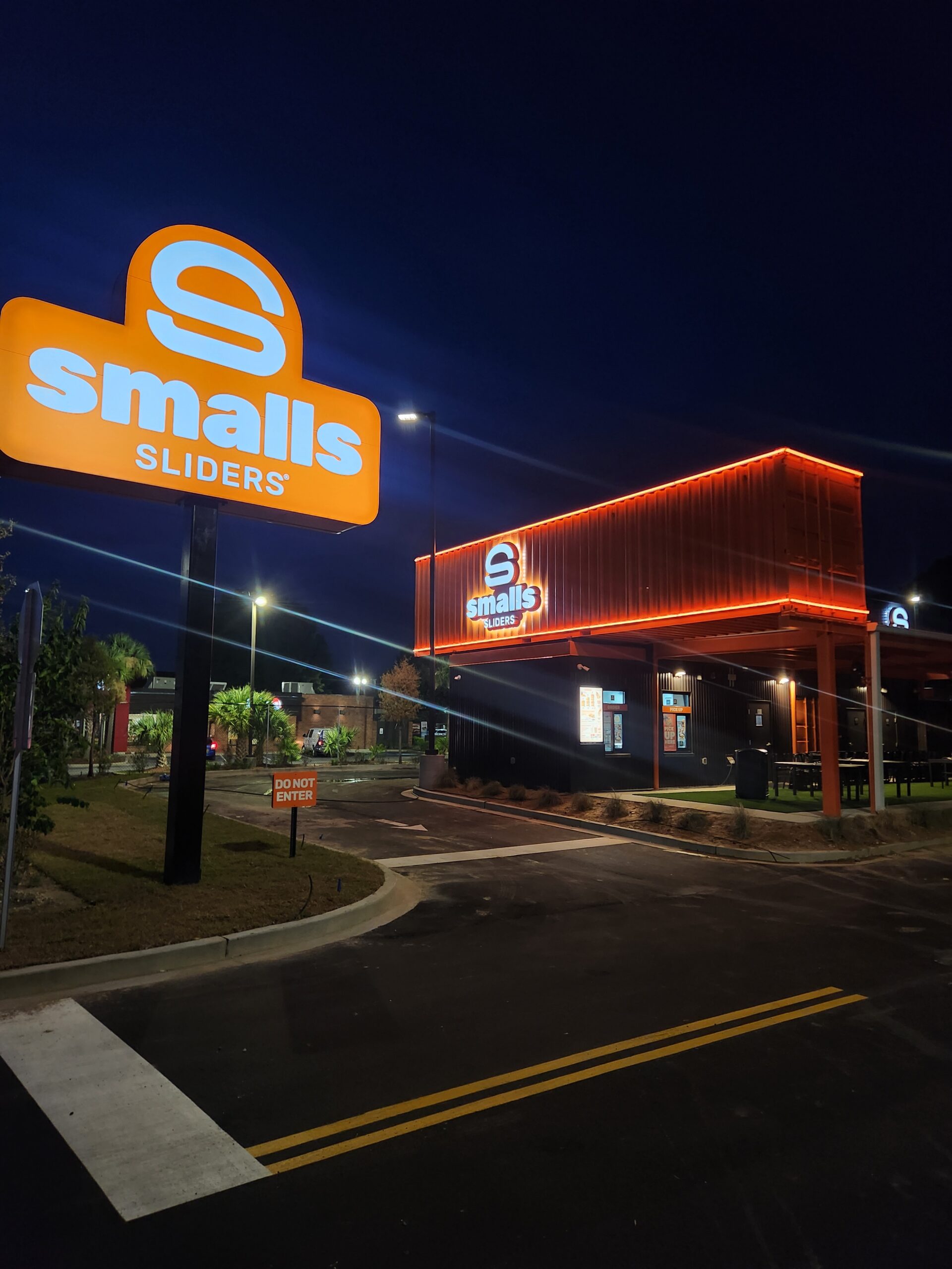 Brightly lit Smalls Sliders restaurant at night showcases the prominent orange sign and modern exterior design. Relevant for local dining options.